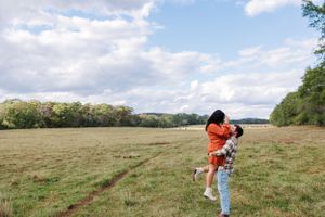 A couple shares a romantic moment in an open field with cloudy skies overhead.