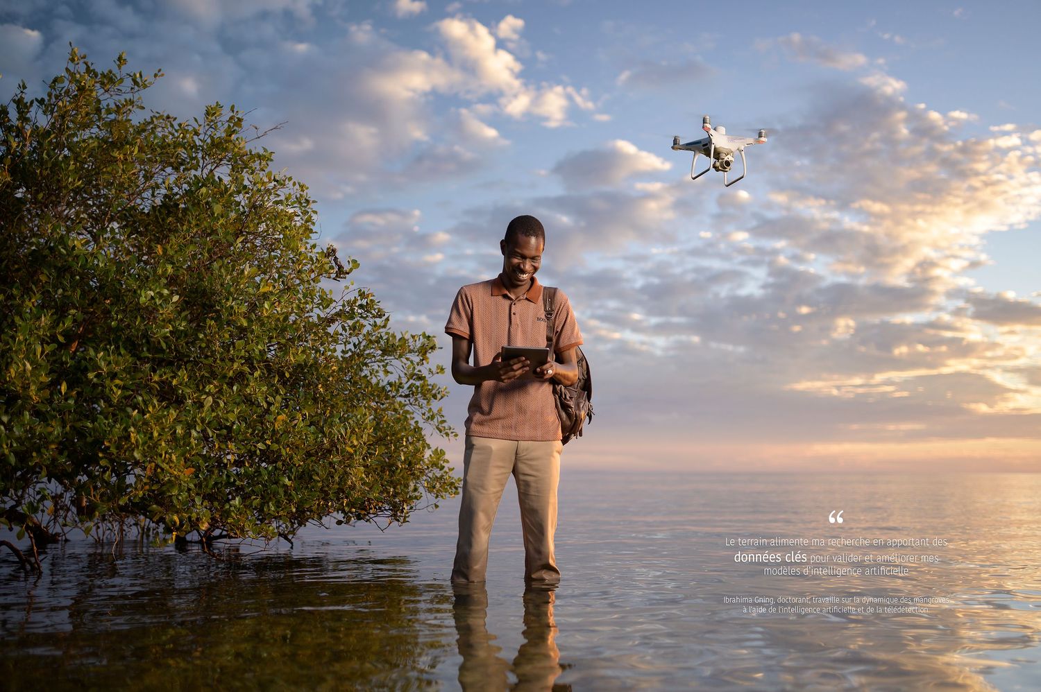 Portrait d'un jeune doctorant sénégalais de l'IRD devant une mangrove, avec un drone volant au-dessus de sa tête.