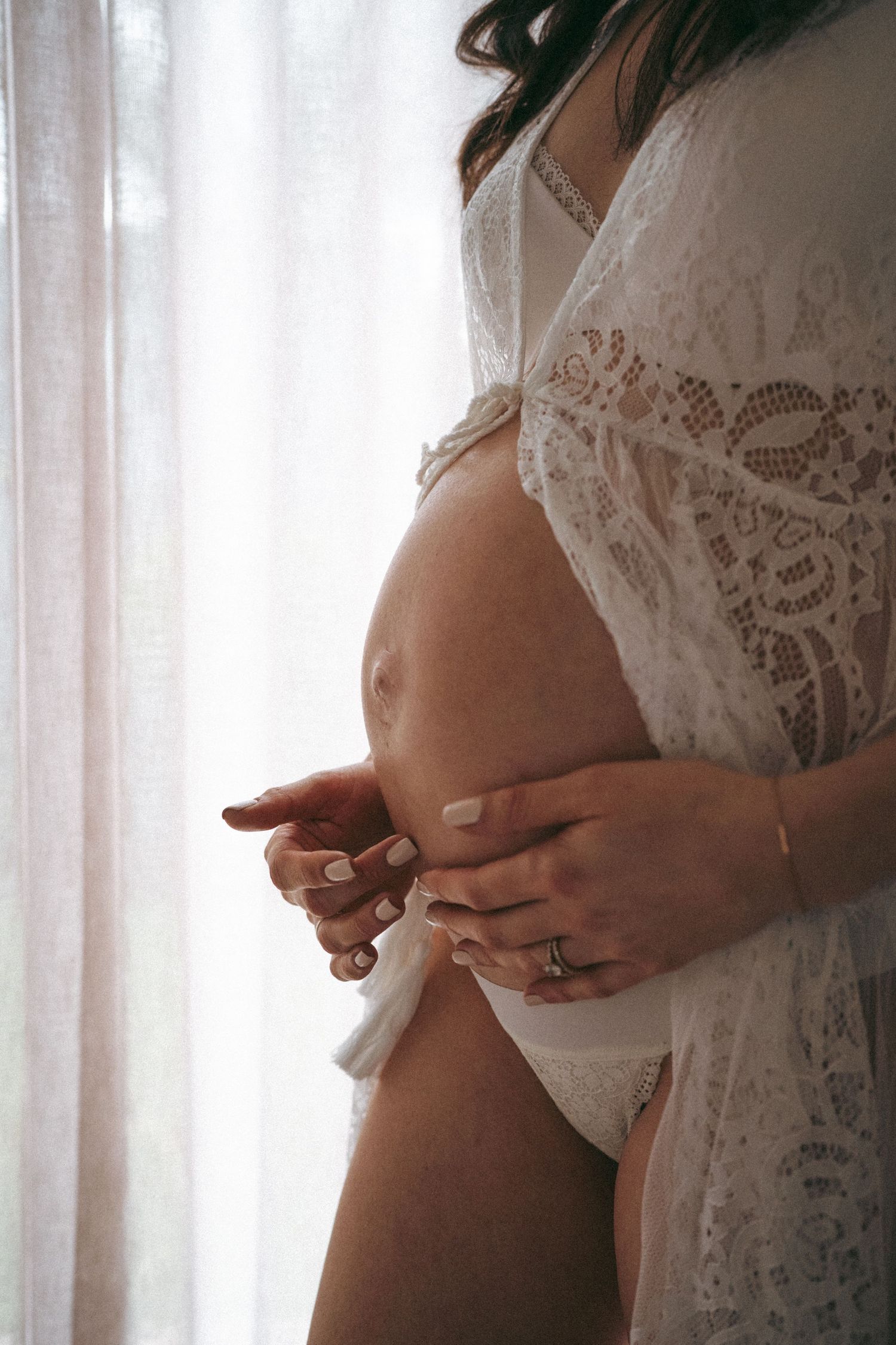 Intimate maternity photos showing a pregnant belly draped in delicate white lace.