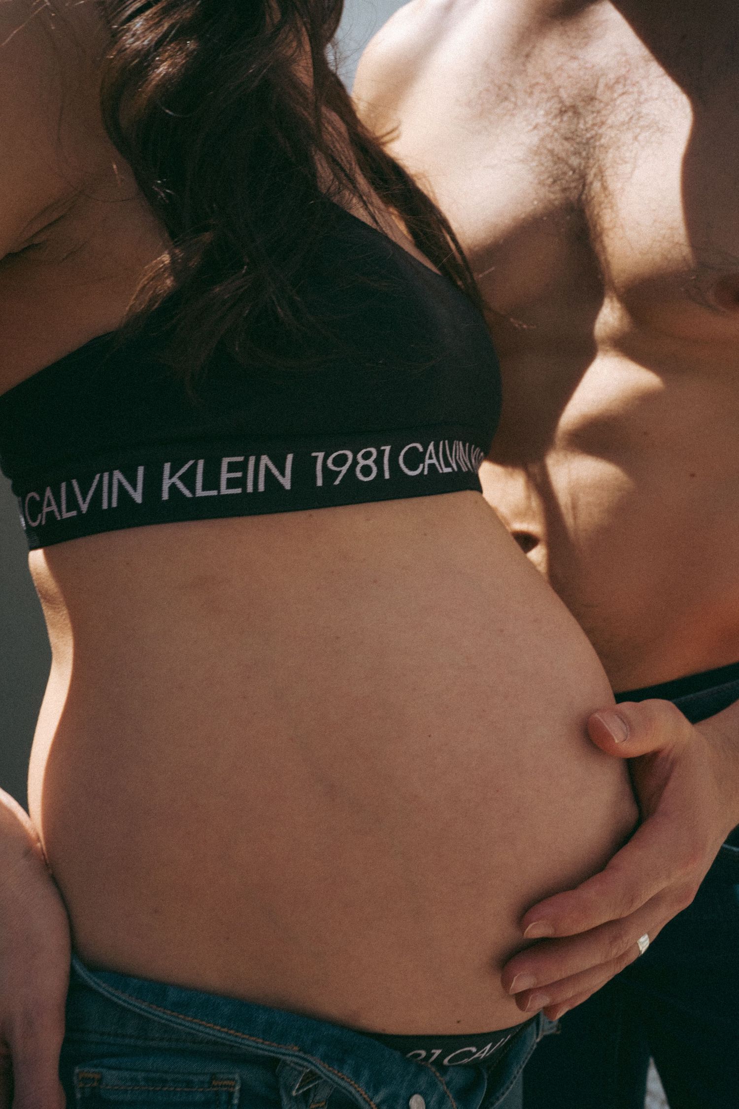 Close-up of a pregnant belly with Calvin Klein sportswear visible in natural lighting.