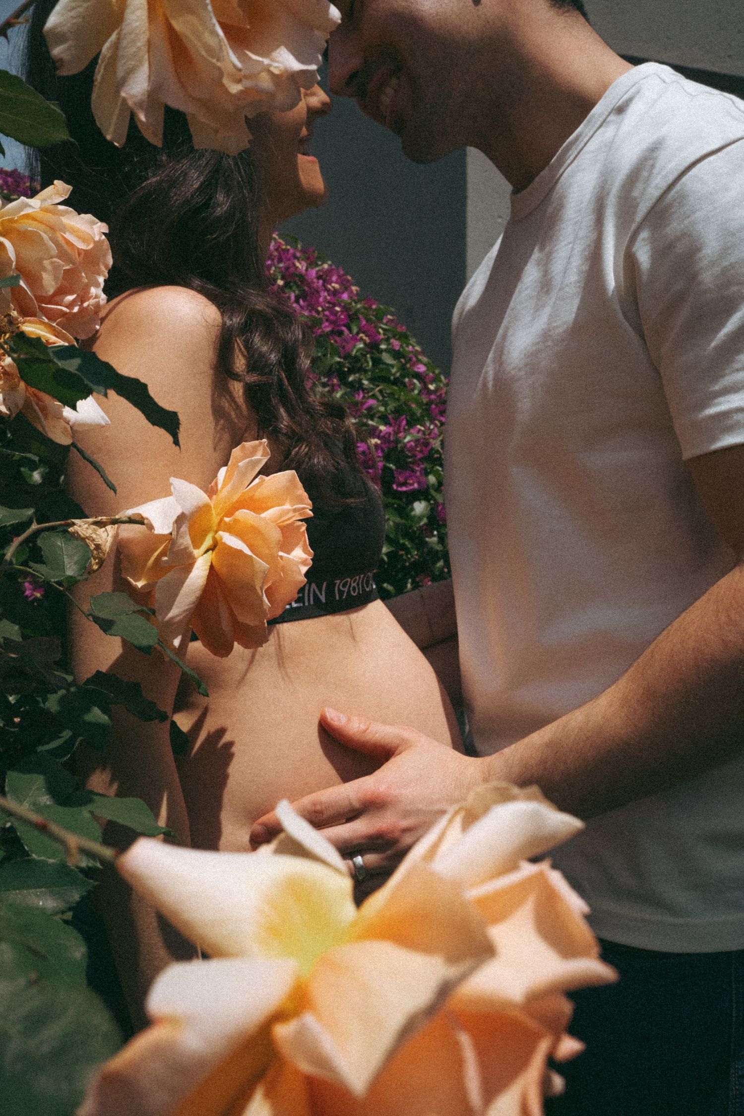 Romantic garden maternity photo with peach roses in soft lighting.