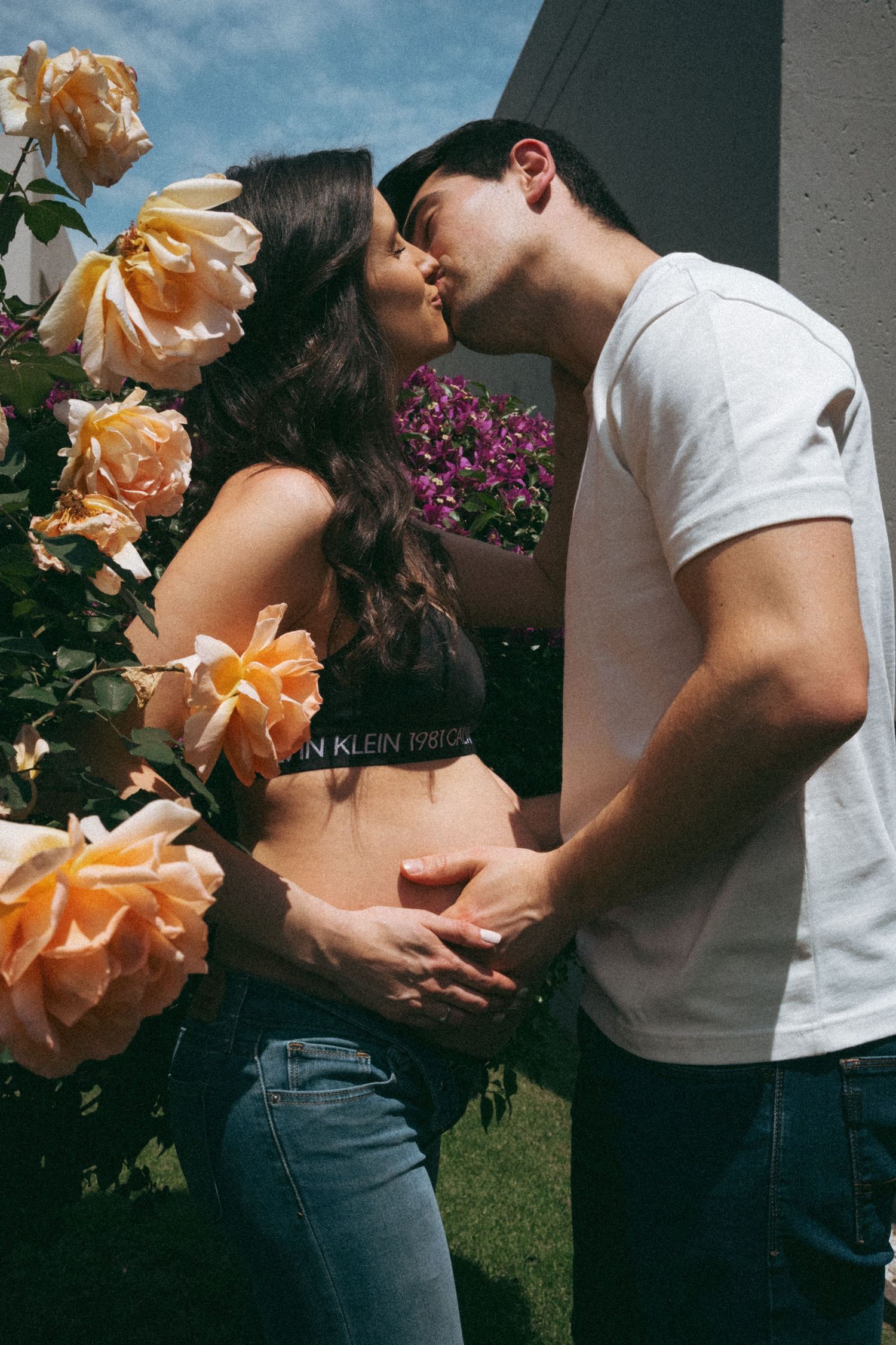 Romantic garden maternity photo with peach roses and tender embrace.