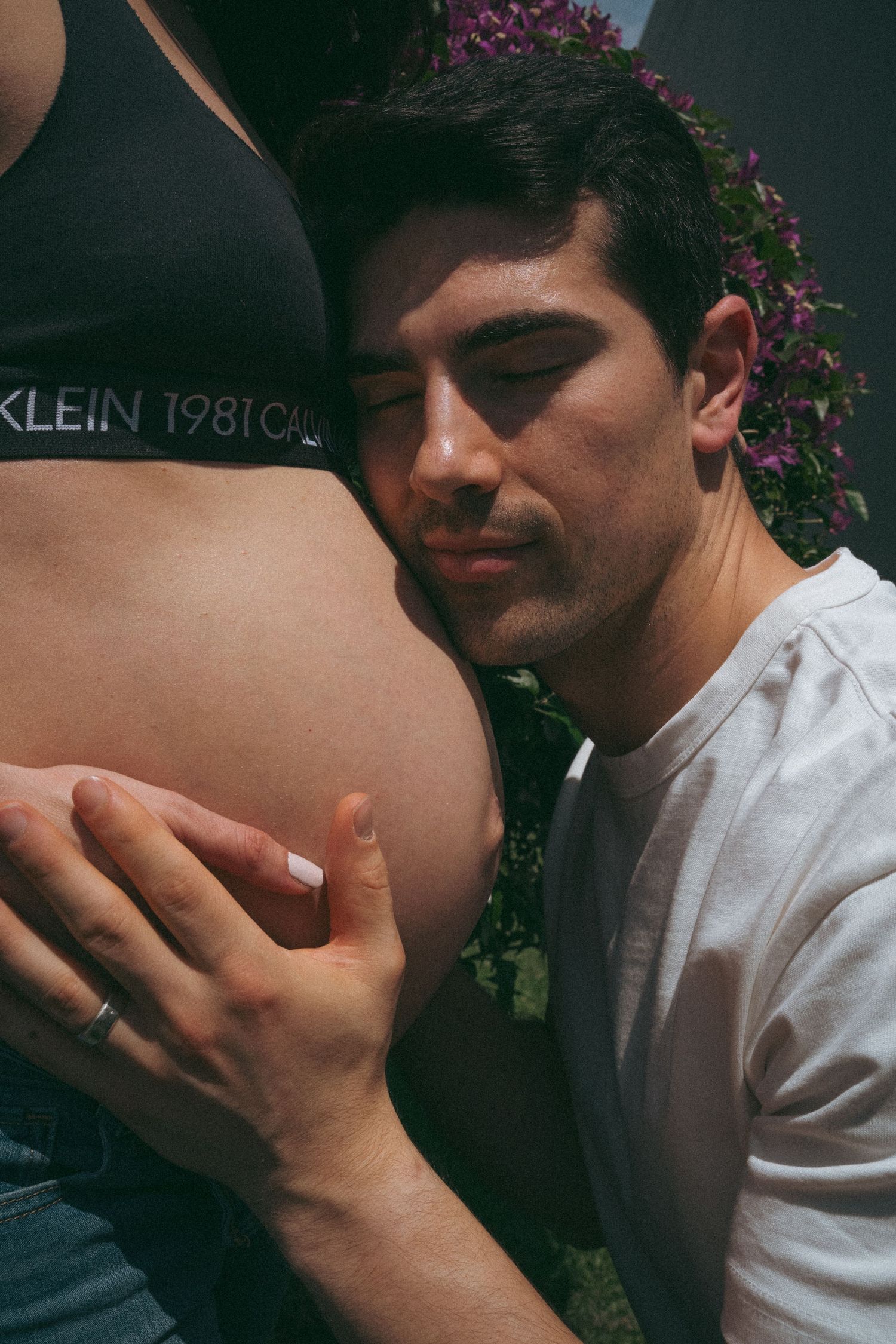 Close-up maternity moment against flowering garden backdrop.