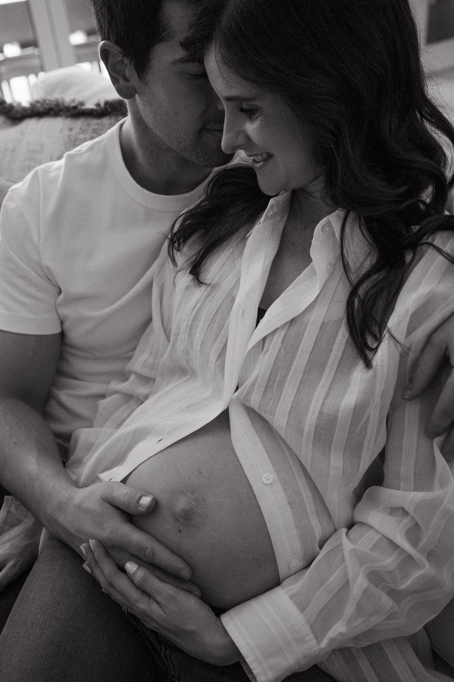 Black and white intimate maternity photo of couple sharing tender moment on couch.