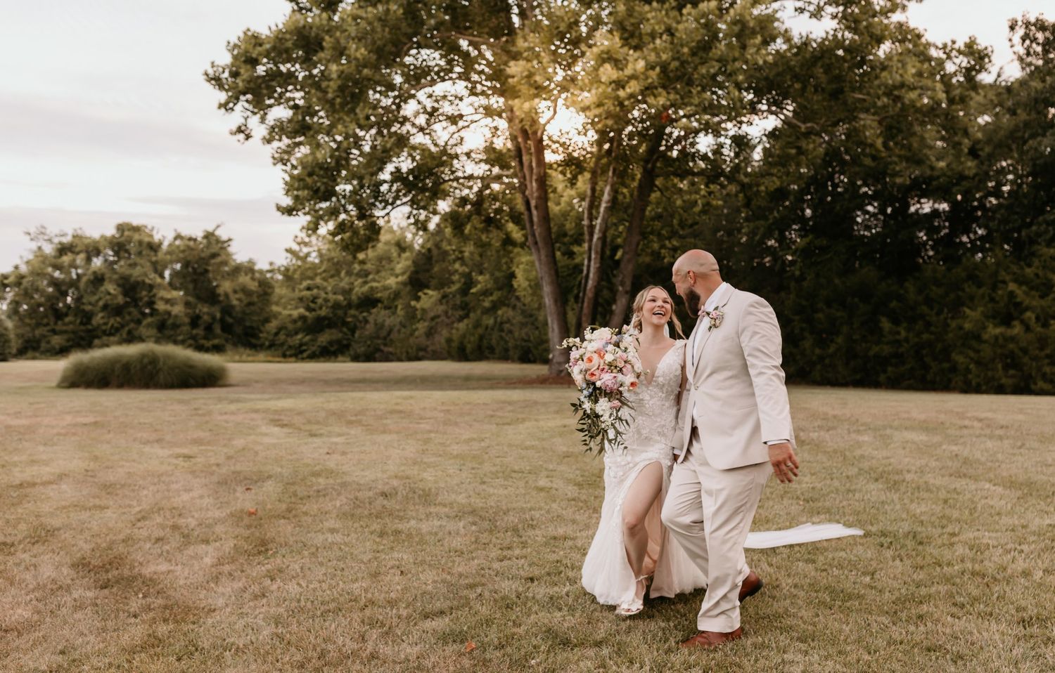 A couple enjoys an intimate moment while walking across a sunlit field at their outdoor wedding.