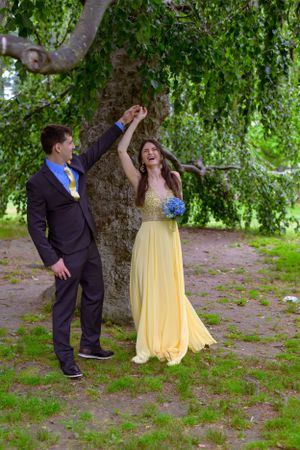 A wedding couple take a dance twirl as they stand between a large ornamental tree canopy.