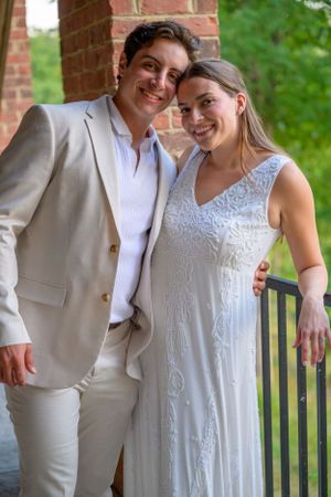 A young wedding couple wearing white and cream colored clothing pose on the deck at sunset.