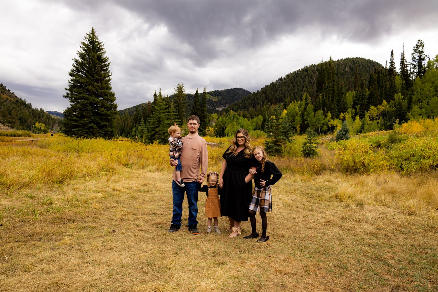 Family gathering in an open field with mountains and pine trees in the background.