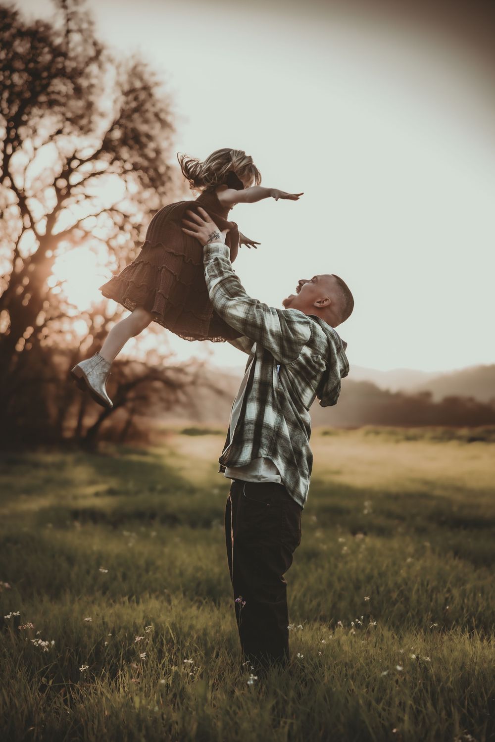 Father lifting young daughter in the air at sunset in a green meadow, sharing a joyful playful moment outdoors.