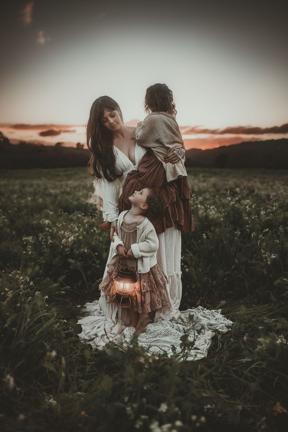 A family sits together in a wildflower field at sunset with a glowing lantern creating a warm, ethereal atmosphere.