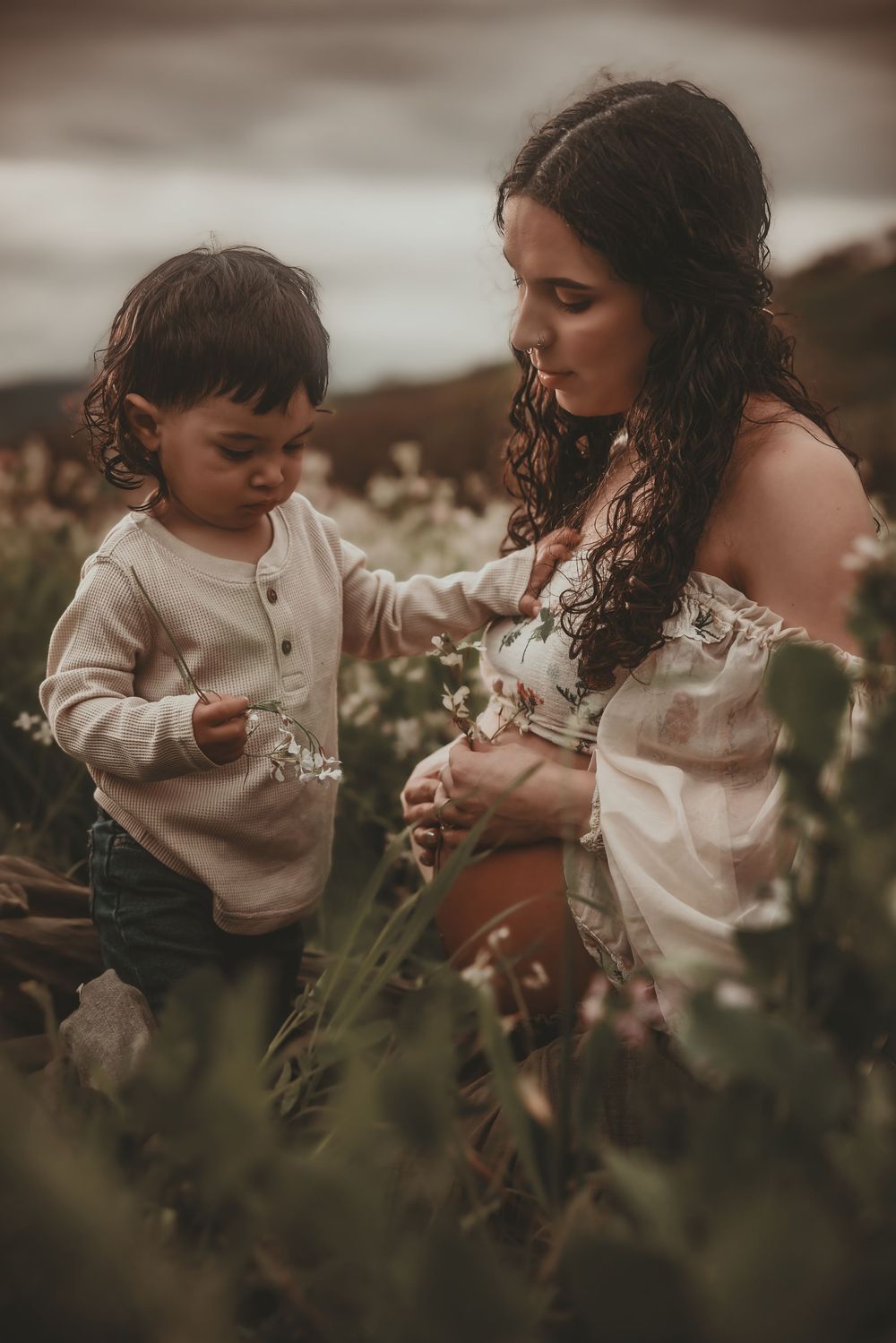 A tender moment captured in a wildflower field with soft lighting and muted brown tones creating a dreamy atmosphere.