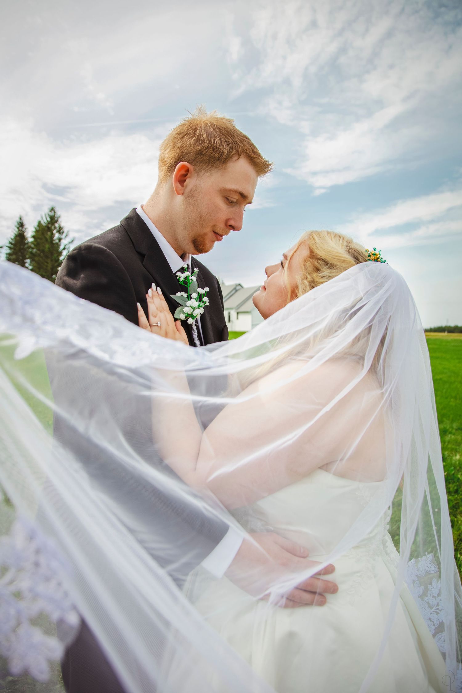 Bride and groom share a romantic moment under flowing white veil outdoors on their wedding day.