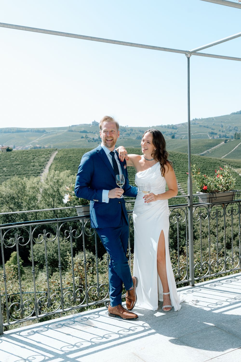 A couple shares a joyful moment on a sunny terrace overlooking rolling hills and vineyards in the countryside.