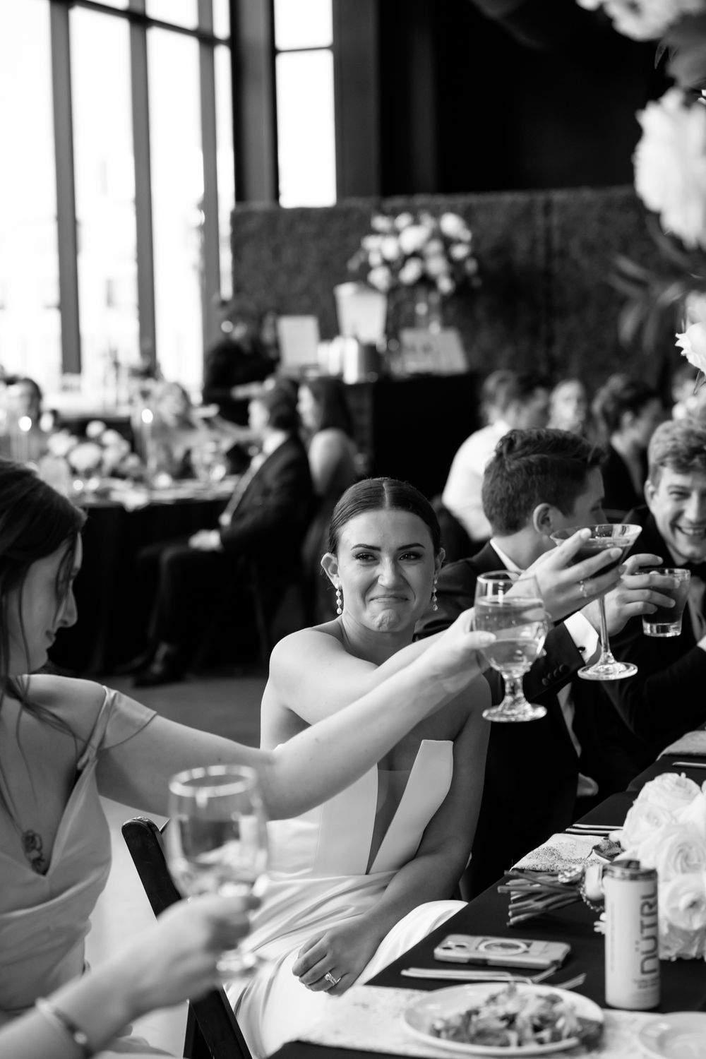 Wedding guests raise their glasses in a toast during a formal reception dinner at an elegant celebration event.