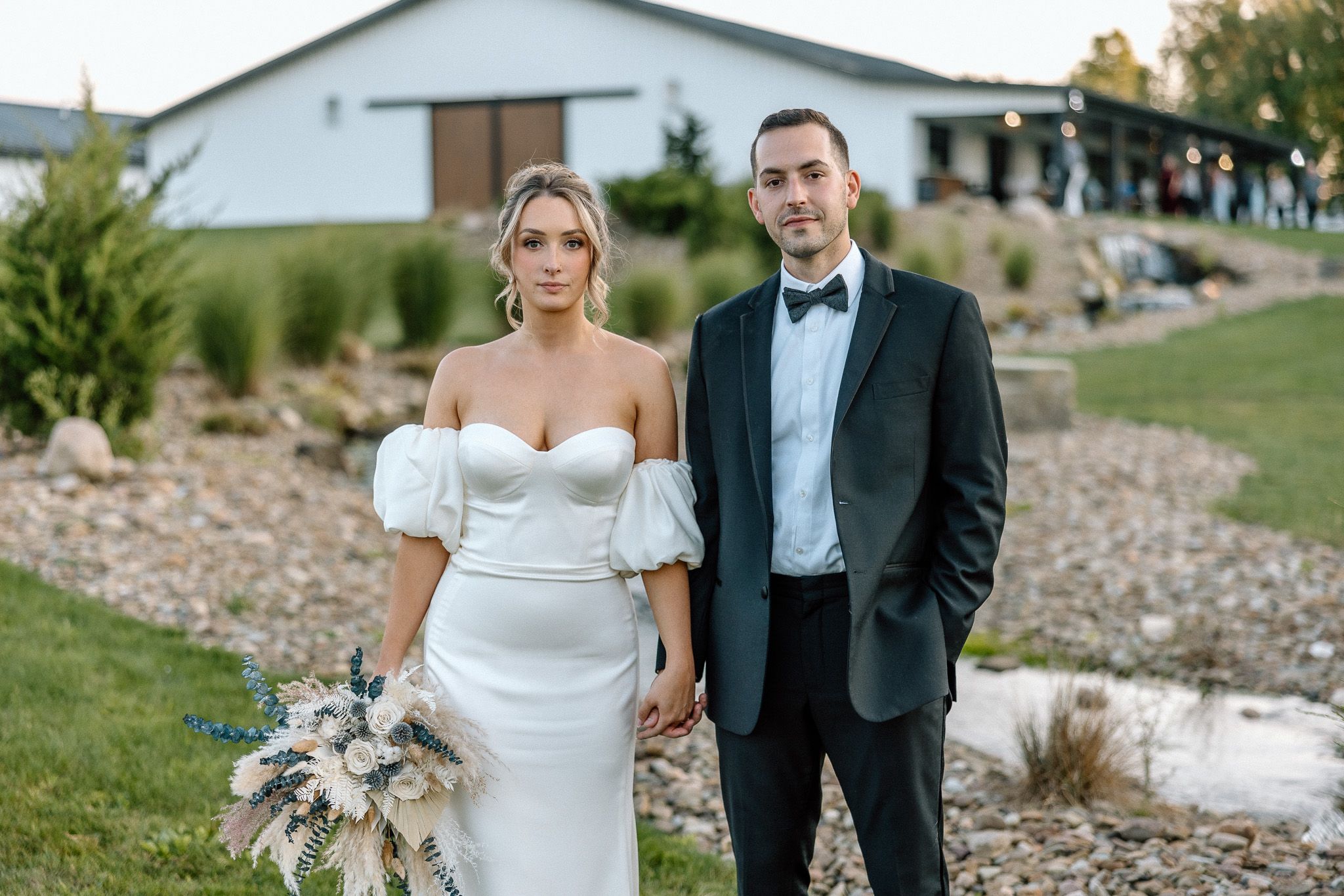 Wedding couple poses in formal attire on landscaped grounds with mountain backdrop.