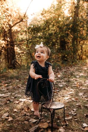 Toddler girl in a navy dress posing in the autumn woods for a family photo session in Branson, MO by L. Ballenger Photography.