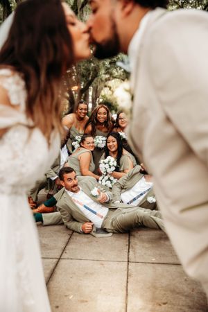Bride and groom kissing while their wedding party cheers in the background, captured by Branson, MO Photographer L. Ballenger Photography.