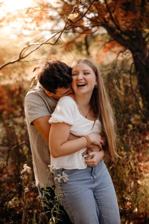 Laughing young couple in a wooded Branson park during an autumn engagement photo session by L. Ballenger Photography.
