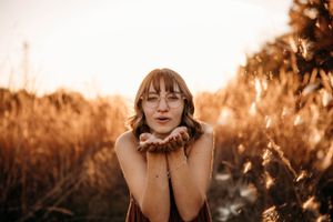 High school senior girl blowing a kiss in a field of tall grass during a sunset photo session in Branson by L. Ballenger Photography.