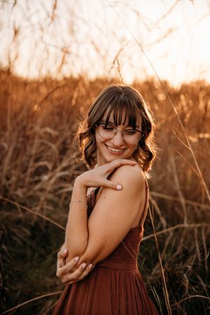 Senior portrait of a girl in a rust-colored dress in a golden hour field, photographed by L. Ballenger Photography.