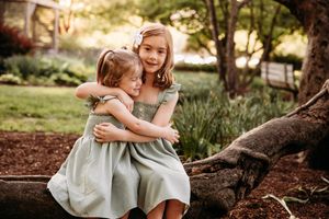 Two young sisters hugging near a fallen log during a woodland photo session in Branson, Missouri.