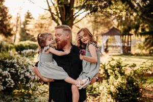 Branson family photographer, L.Ballenger Photography captures a dad hugging his two daughters in a lush garden setting.