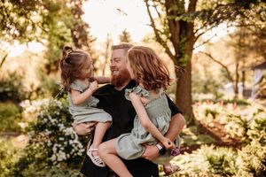 Dad holding his two young daughters during an outdoor family photo session in a Branson, MO park by L. Ballenger Photography.