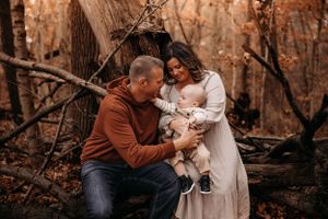Family of three posing in the woods during an autumn photo session in the Branson Ozarks with L. Ballenger Photography.