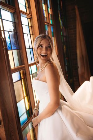 Stunning bride posing by a stained-glass window at a Branson, MO wedding venue by L. Ballenger Photography.