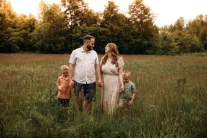 Family of four walking through a wide-open field during a summer photo session in the Branson Ozarks by L. Ballenger Photography.