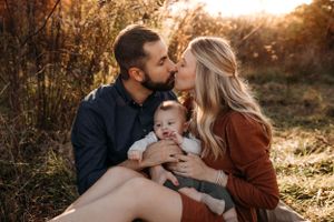 Emotional lifestyle photographer L'Ballenger Photography captures a couple kissing their baby in a glowing fall field in Branson.