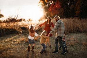 Family of four walking through a field at golden hour during a fall photo session in the Ozarks with L. Ballenger Photography.