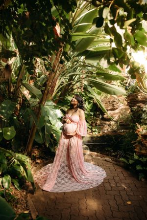 Maternity photo session in a lush tropical garden setting in Branson, MO, featuring a pink gown and L. Ballenger Photography.