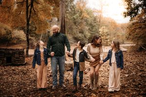 Family of five walking hand-in-hand through autumn leaves for a fall photo session in the Branson Ozarks.