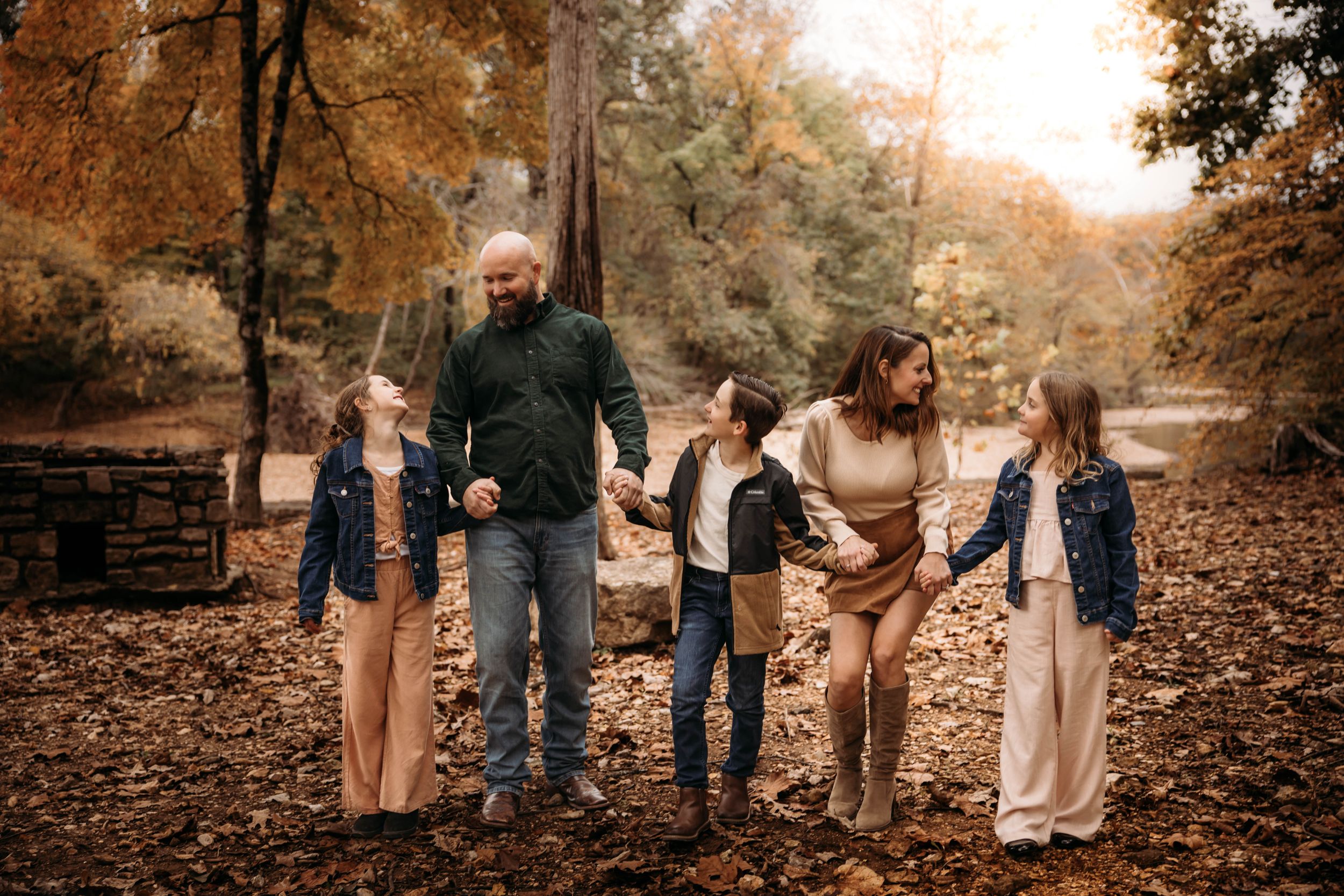 Family of five walking hand-in-hand through autumn leaves for a fall photo session in the Branson Ozarks.