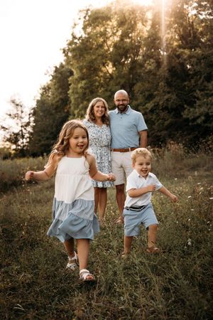 Happy family of four posing in a sun-drenched field for a summer photo session in the Ozarks.