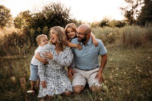 Family of four sitting in tall grass at sunset for a summer portrait session in Branson.