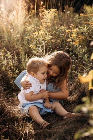 Toddler and older sister laughing in tall grass during a golden hour family photo session in Branson, MO.