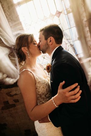 Intimate moment of a bride and groom kissing by a window at a luxury Branson wedding venue, captured by L. Ballenger Photography.