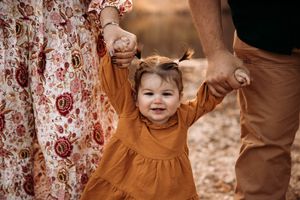 Close-up of a toddler girl in an orange dress walking during a fall family photo session at Stockstill River in Branson, Missouri.