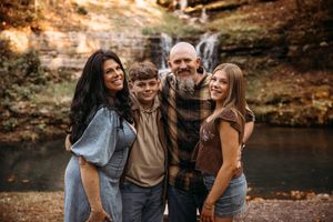Family of four posing near the rocky shoreline of a Branson Missouri creek in the fall.