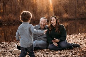 Family of three sitting on a bed of fall leaves during an autumn photo session in the Ozarks.