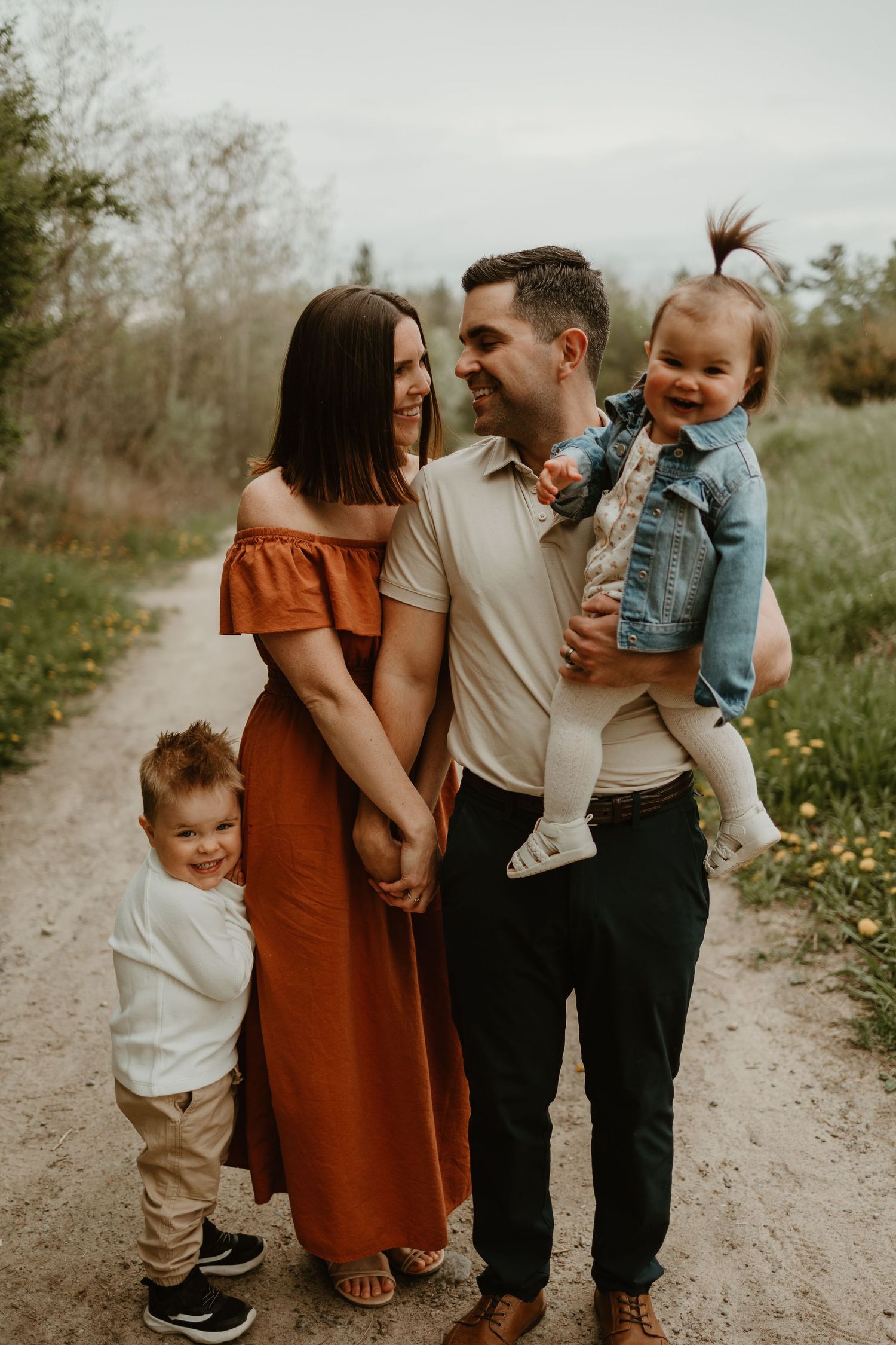 A family in coordinated outfits shares affectionate moments on a dirt path during a photo session.