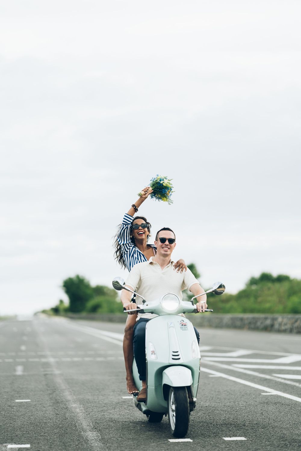 A couple rides together on a white scooter along an empty road while enjoying a romantic moment.