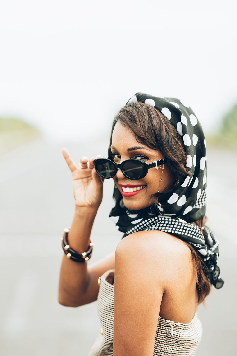 A stylish black and white polka dot headscarf paired with a striped top and sunglasses creates a chic summer look.
