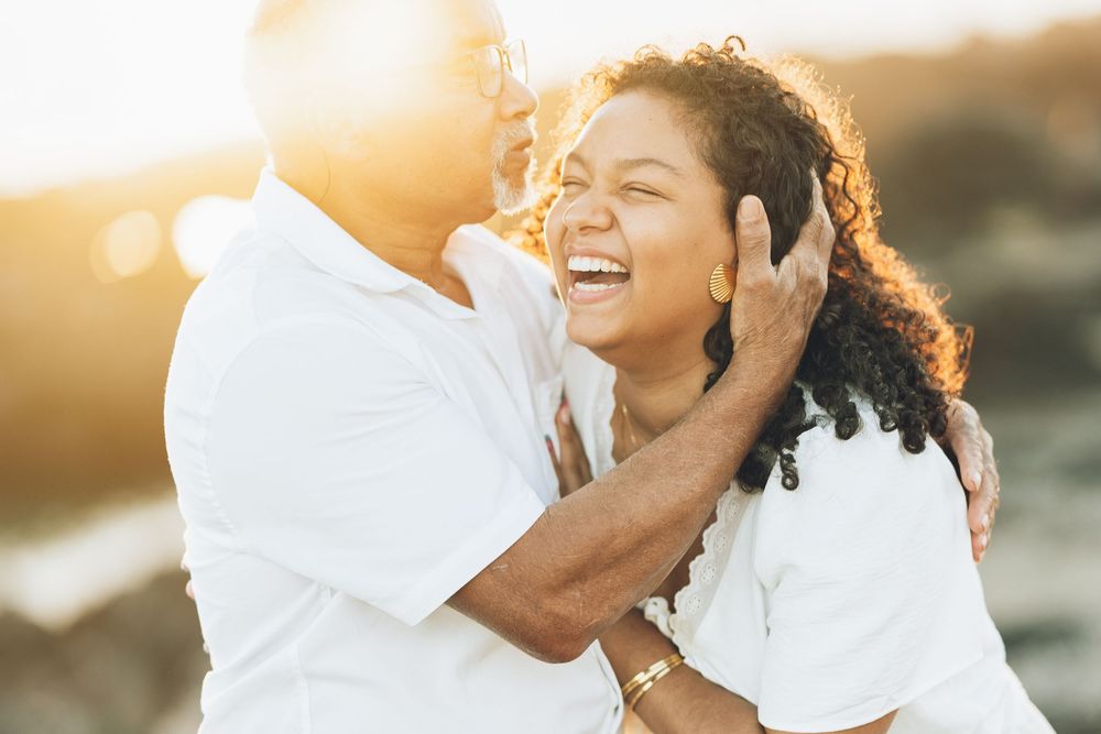 Couple embraces during a romantic golden hour photo session by the beach at sunset.