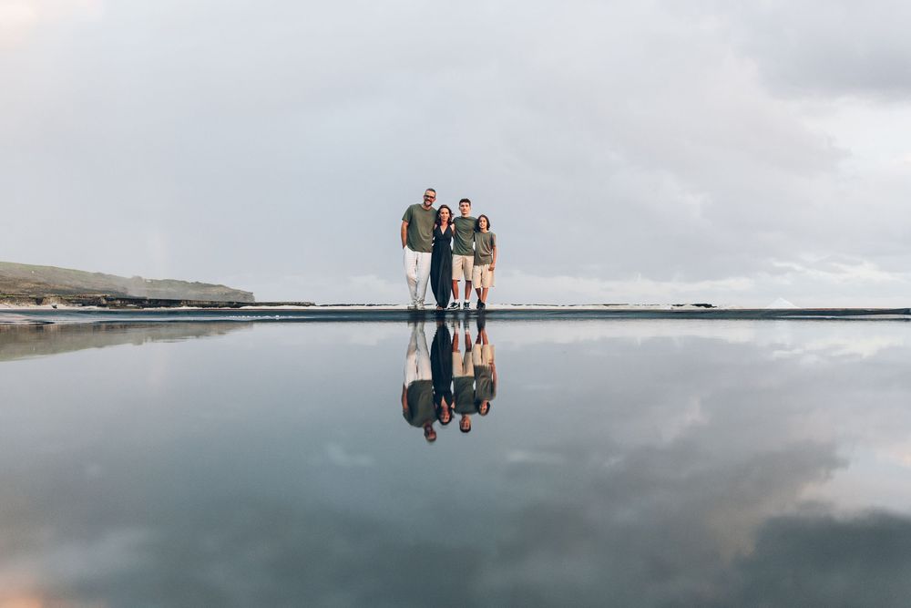 Family of four standing on reflective black sand beach with dramatic cloudy sky in Iceland.