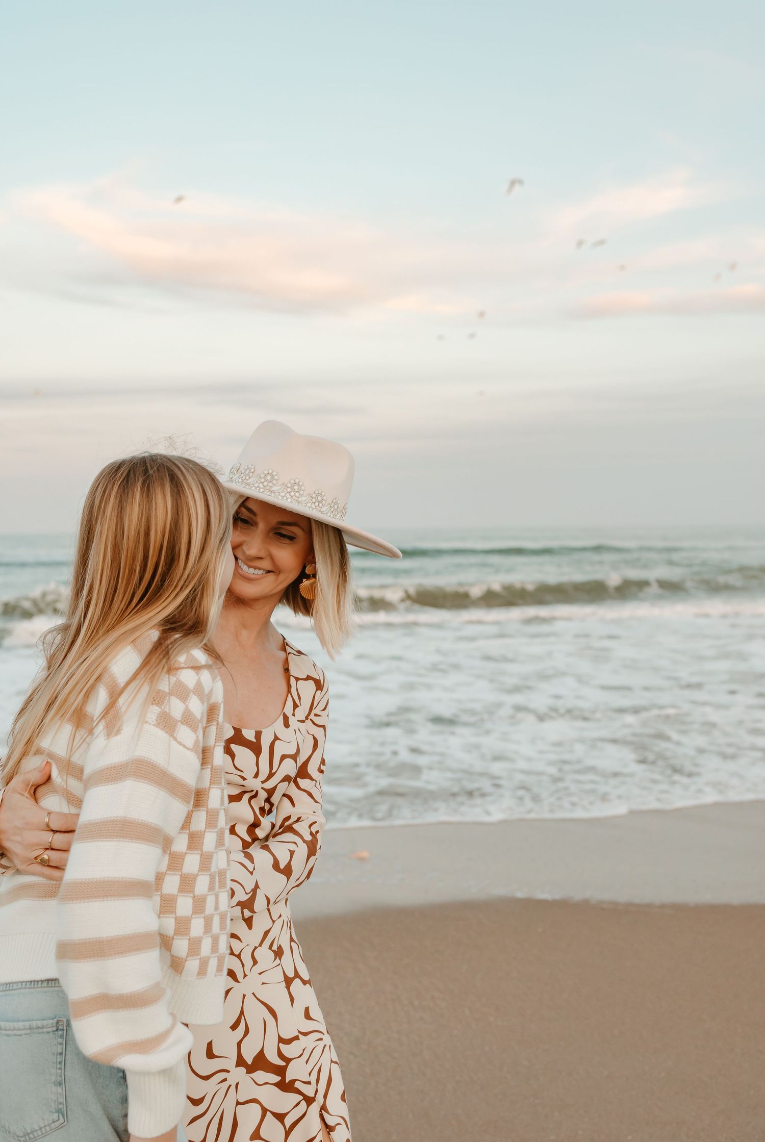 Family embracing on beach at sunset wearing coordinated neutral tones.