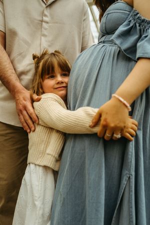 A series of images showing hands holding onto a child in a beige sweater standing between adults in gray and khaki clothing.