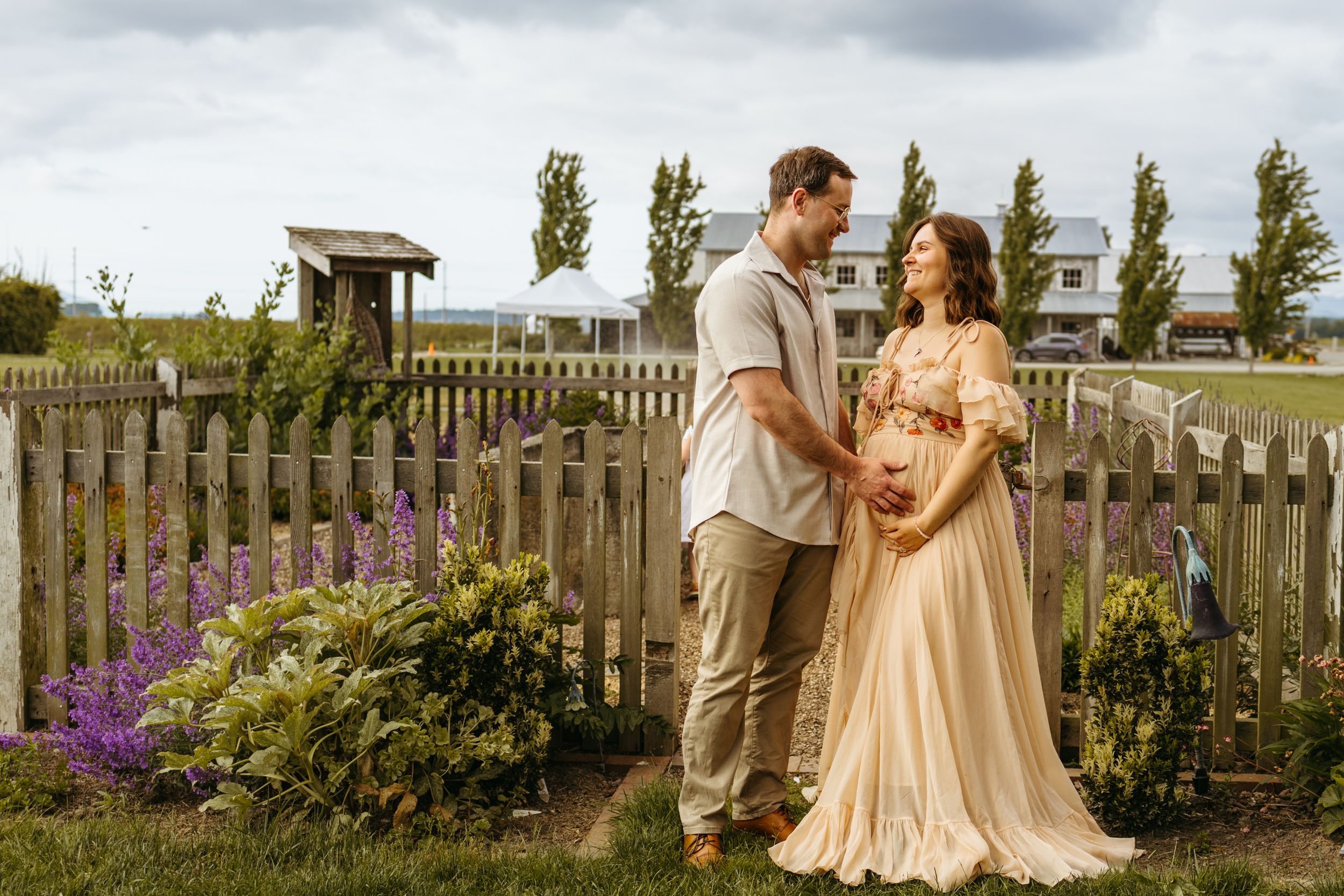 A tender rustic outdoor wedding moment captured between a bride and groom in a garden setting with sunlit wooden fencing.